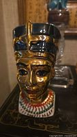 Front view of the ceramic decanter featuring Queen Nefertiti bust with gold face paint and detailed headdress.