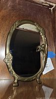Front view of oval tabletop mirror with floral and woman figurine metal frame.