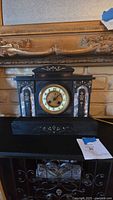 Front view of black onyx mantel clock showing clock face, marble columns, and gold decorative detailing.