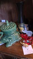 Front view of collection including green ceramic elephant basket with lid, tall black wood vase with gold elephants, red glass elephant, frosted glass elephant, mini brass elephant on wooden surface