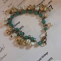 Elephant-themed charm bracelet showing details of gold-tone elephant charms, natural freshwater pearl beads, and green natural stone beads, clasp visible.