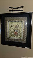 Framed silk embroidery artwork hanging on wall showing floral and butterfly design.