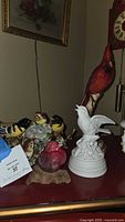 Photo showing all four bird figurines together: tall red cardinal, white bird figurine, red songbird on wood base, and yellow orioles family.