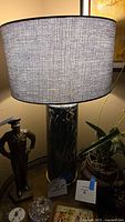 Column table lamp with black and white marbled base and grey fabric drum lampshade on a wooden surface, surrounded by decorative items.
