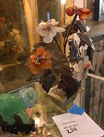 Overview of multicolored jade flower arrangement with white and orange flowers and dark leaves alongside green jade elephant figurine on black base