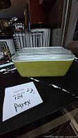 Yellow Pyrex rectangular refrigerator dish with clear glass lid shown from front angle on black countertop, with note showing item number and brand.