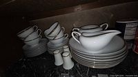 Photo of Royalton China Golden Elegance teacups, saucers, plates, sugar bowl, creamer, salt and pepper shakers stacked on a dark counter under a cabinet.