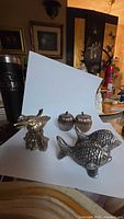 Photo of two pewter birds set on a floral handled holder alongside the apple or pumpkin shaped shakers and a single fish shaker.