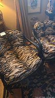 Photo of two tiger print upholstered armchairs with black wood frames, showing the seat cushions and armrests.