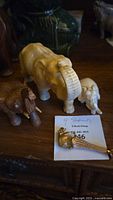 Photo showing all four elephant figurines including a medium tan resin elephant, a smaller cream resin elephant, a brown wood elephant, and a small gold-tone metal elephant.