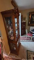 View of tall two-piece wooden display cabinet with glass doors showing upper and lower sections, carved wood, and glass shelves.