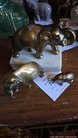 Three bronze or brass elephant figurines with the largest on a white marble base, showing varying sizes and visible polish residue on one.