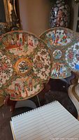 Two Oriental decorative plates on cherry wood plate stands showing full plate and backplates