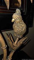 Close-up of cast metal parrot figurine with detailed feathers perched on bamboo motif stem