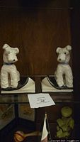 Pair of white ceramic dog-shaped bookends with blue collars, shown side by side on a shelf.