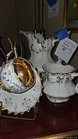 Photo showing white porcelain tea set items including creamer, cup, and saucer with gold filigree and gold accents
