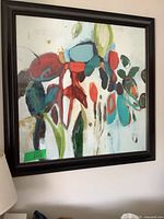 Framed abstract floral art print on wall, showing vibrant colors and dark wooden frame.