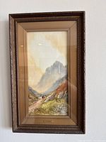 Framed watercolor painting showing a mountainous landscape scene with path, cows, and person. The frame is brown and textured, size approximately 12x18 inches.
