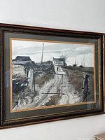 Framed rural landscape print hung on a white wall, showing the full view with ornate dark wood frame and glass cover