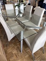 Side view of glass dining table with six matching chairs upholstery in light color and metal legs