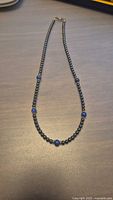 Full view of necklace laid flat showing the length and arrangement of gunmetal hematite beads and blue lapis lazuli beads.