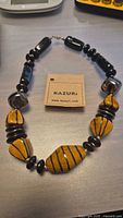 Kazuri handmade necklace with alternating yellow striped and black clay beads laid flat with a brand tag in the center