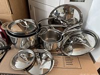 Various Lagostina stainless steel pots and pans with glass and metal lids shown stacked and arranged, showcasing the collection's overall condition and appearance.