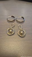 Two pairs of sterling silver earrings on flat surface, one hoop pair and one drop style pair with round beads.