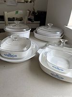 Photo showing multiple Corning Ware baking dishes with the distinctive blue floral corning ware design and clear glass lids, arranged on a surface.