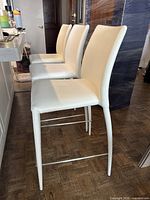 Three white faux leather bar stools aligned near a countertop showing overall look and style.