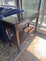 Angled front view of console table showing glass top, wood frame and lower shelf