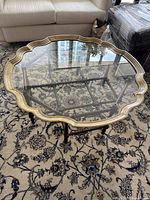 Top view of the scalloped glass top coffee table showing clear glass with gold frame and reflection of ceiling.