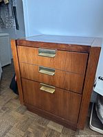 Front and angled view of the 3-drawer wooden side table showing brass hardware and wood grain.