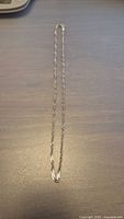 Full view of the thin sterling silver rope chain necklace lying flat to show length and clasp.