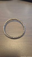 Front view of the twisted cable sterling silver bangle bracelet laid flat on a table, showing circular shape and smooth finishes.