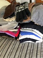 Overview of folded women's clothing tops, gloves, and scarves stacked on a surface.