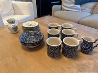 Photo shows 6 ceramic mugs with dense blue floral pattern, 1 creamer pitcher with similar blue floral pattern, 4 bowls with dense blue floral pattern, and 8 white saucers with blue floral accents and gold rims.