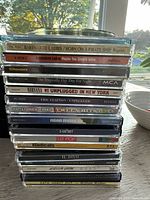 Stack of 26 music CDs showing a variety of artist names and album titles visible on the spines including Barenaked Ladies, The Tragically Hip, John Mayer, Nirvana, U2, and others.