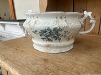 Side view of antique ceramic wash basin showing embossed floral pattern, gold accenting, and ornate handle
