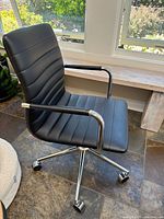 Side angle view of black faux leather office chair showing seat, armrest, and wheels on chrome base.