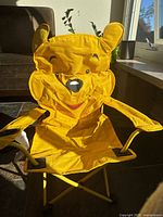 Front view of foldable yellow Disney toddlers lawn chair with Winnie the Pooh face design and ears on backrest.