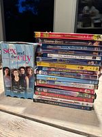 Stack of DVDs and VHS tapes showing titles from Sex and the City box set, Disney and other animated movies.