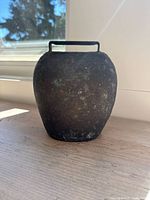 Front and side view showing the shape, size, and patina of the cast iron cow bell with an integrated handle on top.