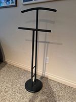 Full front view of black metal freestanding valet stand showing curved top bar and horizontal bar for hanging clothes
