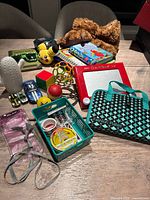 Photo showing collection of kid's toys, plush toys, Minecraft sunglasses, books, small toy cars, and craft items arranged on a table