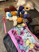 Wide view of yarn balls in assorted colors, silk thrums, knitting needles and decorative bag on floor