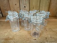 Seven clear glass clip-top jars with metal locking lids on wooden surface.