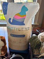 Shows unopened bag of Pretty Litter in lotus flower scent with part of plush toy and yarn basket visible
