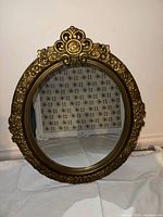 Front view of the oval wall mirror showing the floral embossed antique gold resin frame with detailed design and crest at top