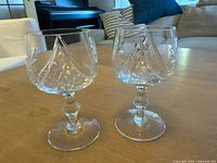 Photo shows two small cut crystal wine goblets with diamond and fan cut patterns on the bowls and faceted stems, placed on a wooden table.